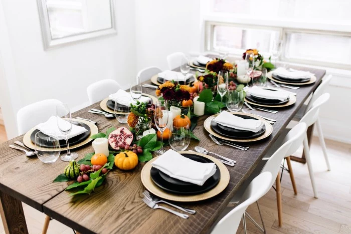 thanksgiving dinnerware, long wooden rectangular table, set for eight people, pale beige and black plates, glasses and silver cutlery, decorative pumpkins, leaves and fruit 