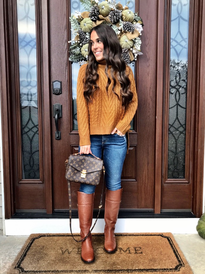 cable knit jumper in orange, worn with blue skinny jeans, and tall brown leather boots, by a smiling brunette woman, holding a designer bag,thanksgiving outfits for women