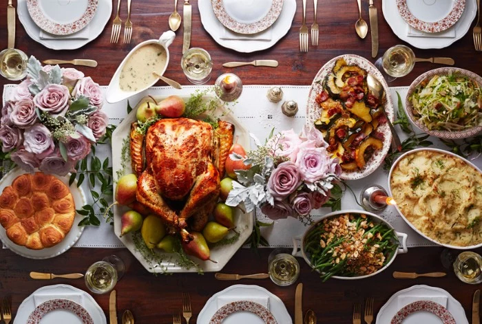 pale pink roses, in two small bouquets, placed on a table, featuring a roasted turkey, mashed potato and other dishes, thanksgiving text messages, plates and cutlery for six people