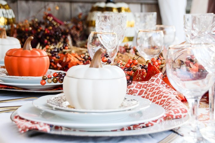 pots in the shape of pumpkins with lids, in white and orange, thanksgiving table decorations, plates and glasses, decorative fall leaves and berries