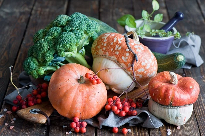 berries on small thin branches, several pumpkins in strange shapes, broccoli and a gourd, happy thanksgiving wishes, mortar and pestle with herbs nearby