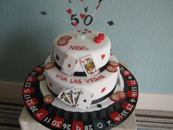 roulette and gambling chips, made from black and red fondant, decorating a white cake, with a 50 topper, dice and playing card symbols, 50th birthday party ideas for men, las vegas casino