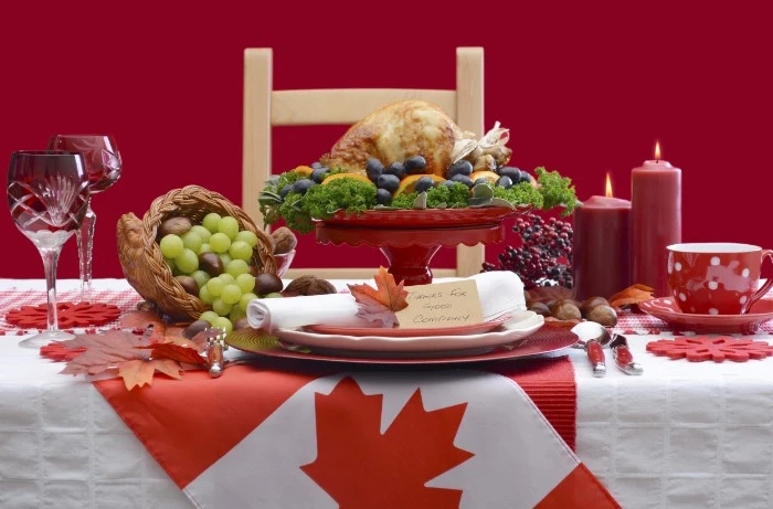 flag of canada, decorating a table, with a roasted turkey, grapes and two lit candles, thanksgiving message to employees, plates and wine glasses, a coffee cup and a saucer