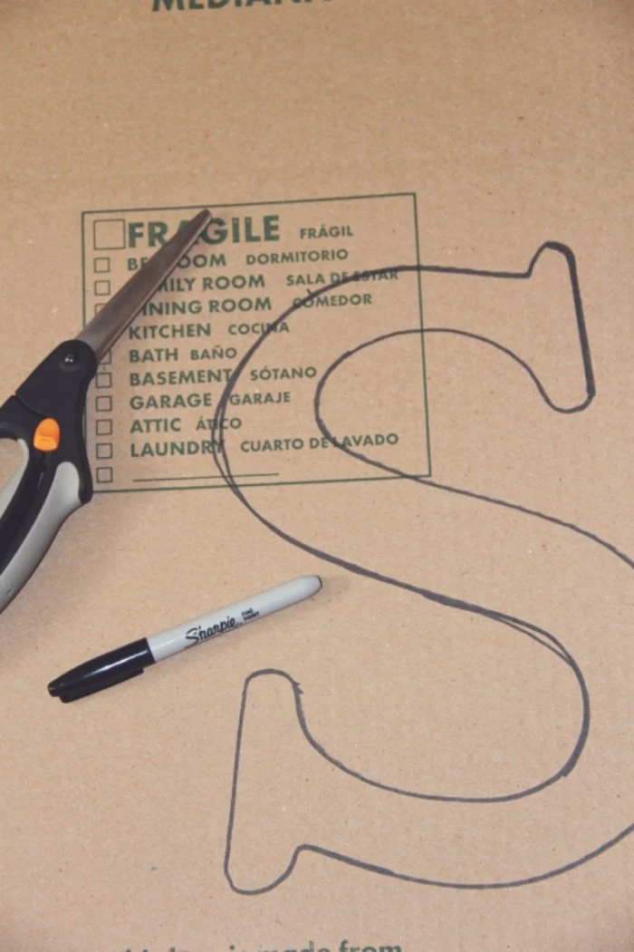 pair of scissors, and a black marker, placed on top, of a piece of beige cardboard, teenage girl room ideas, with the letter s, drawn on it in black