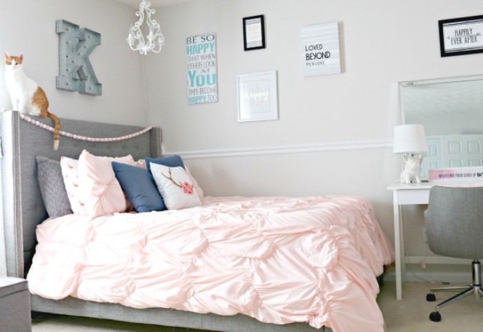headboard in grey, attached to a bed with multiple cushions, and a pale powder pink bed cover, cool beds for teens, posters and a desk, with a grey chair