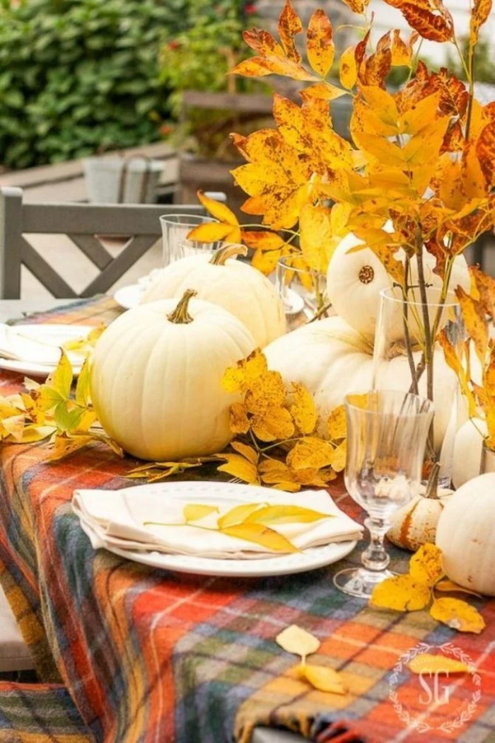 blue and grey, red and orange plaid tablecloth, on a table, decorated with white pumpkins, and yellow fall leaves, white plate and napkin, glass and vase