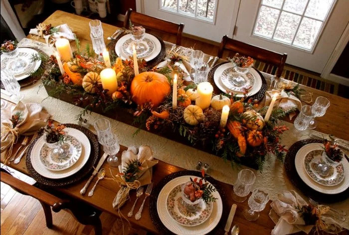 table set for six, and decorated with a long and narrow wooden crate, containig pumpkins and candles, gourds and fruit, and leaves in different colors, thanksgiving centerpiece, on a rectnagular wooden table