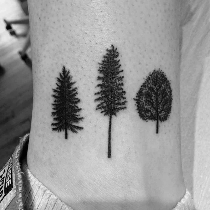 three small tattooes of different trees, done in black ink, on a man's ankle, seen in close up