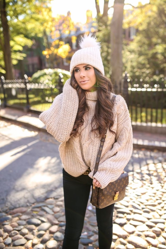 fluffy pom pom, on a pale cream knitted hat, worn by a young brunette woman, with long curled hair, thanksgiving outfits, oatmeal chunky knit jumper, black skinny jeans, and a designer shoulder bag
