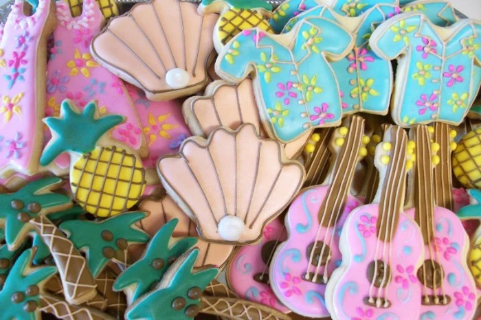assortment of cookies, shaped like shells and dresses, guitars and pineapples, shirts and palm trees, decorated with colorful frosting and edible pearls, 50th birthday colors