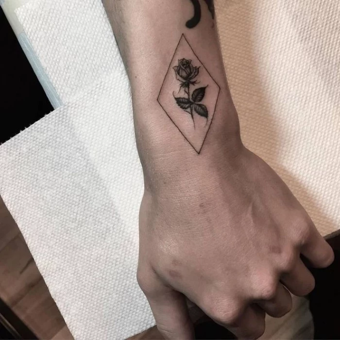 diamond shape drawn in black, containing a rose, with four leaves, forearm tattoos, on the upper side of a man's wrist