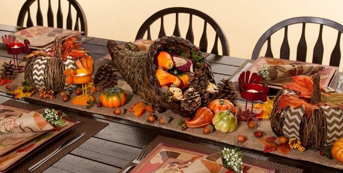 wicker decorations shaped like two pumpkins, and a cornucopia, filled with gourds, pinecones and nuts, on a dark brown wooden table, thanksgiving tablescape, acorns and orange fall leaves