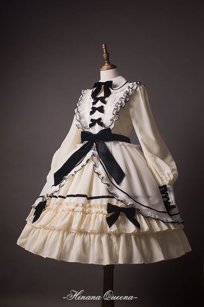 define lolita, dress in white and cream, decorated with multiple black bows, and featuring frills, a peter pan collar, and a lace bib detail