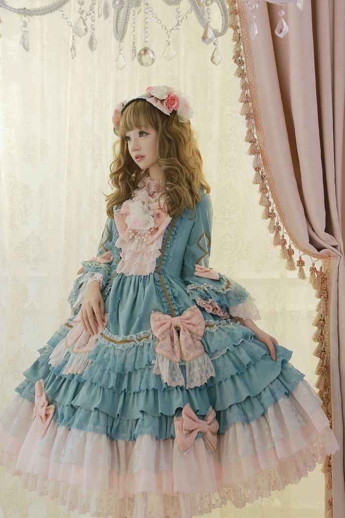 baroque inspired dress, in pale blue, with a tiered skirt, light peach pink bows, and lots of white lace, worn by a pale and slender girl, with light brunette hair