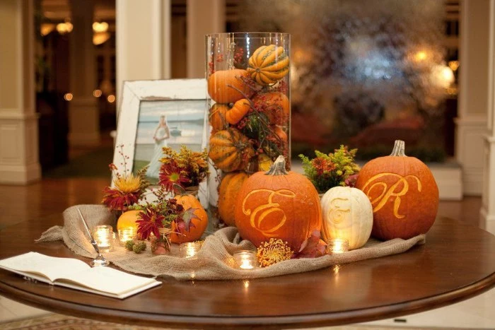 tea lights and flowers, and tiny orange pumpkins, surrounding three bigger pumpkins, with the letters e and r, and the sign & engraved on them, cheap centerpiece ideas, on a round dark brown table