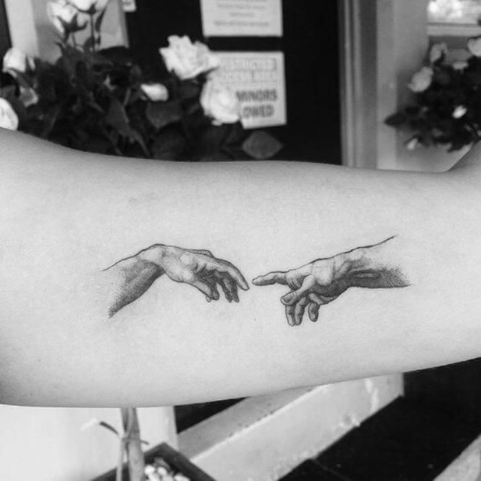 classical art-inspired forearm tattoos, the hands from michelangelo's the creation of adam, tattooed on a person's arm, with black ink