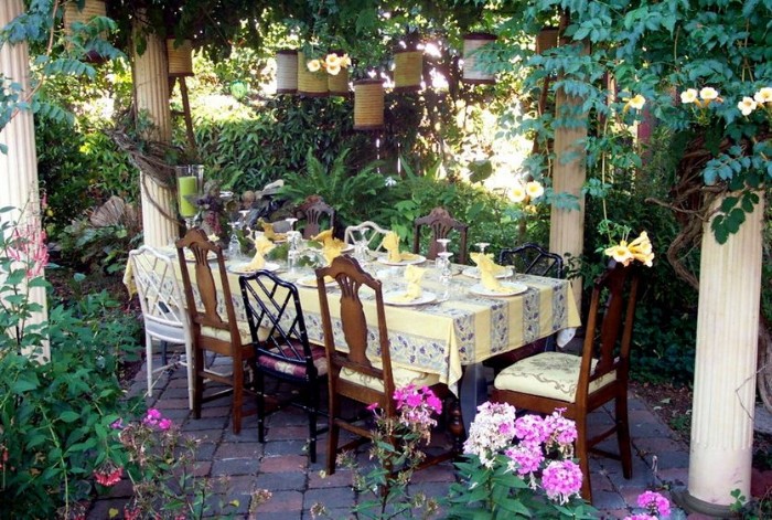 flowers and other plants, and several white columns, surrounding a festive table, with several different chairs, 50th birthday party ideas for mom, dinner in the garden