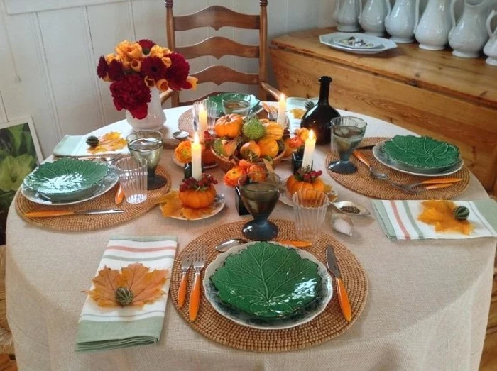 green dishes shaped like cabbage leaves, on a round table set for four, cutlery with orange handles, red and orange flowers, pumpkins and fruit