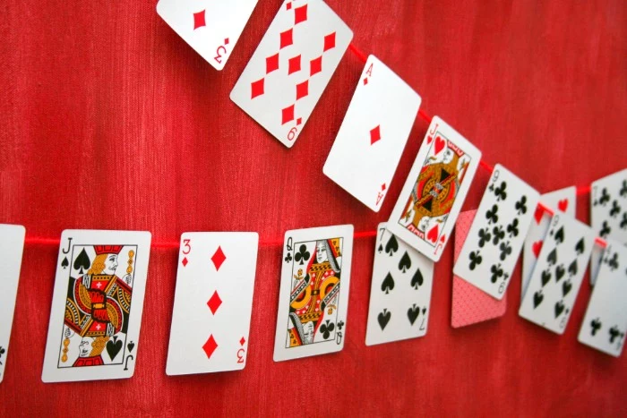 two garlands made from playing gards, stuck onto pieces of red thread, and hung on a red curtain, 50th birthday party ideas for men, poker night theme