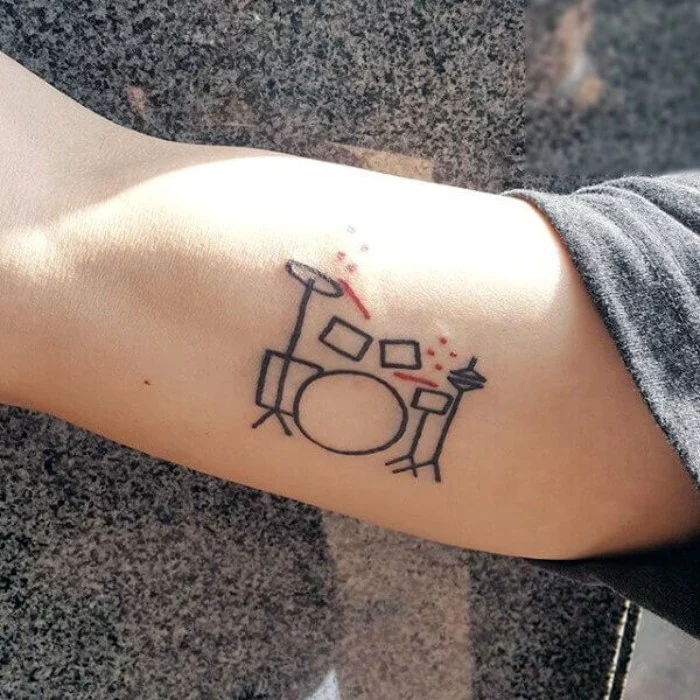doodle tattoo in black and red, depicting a drum kit, cool arm tattoos, done on a person's upper arm