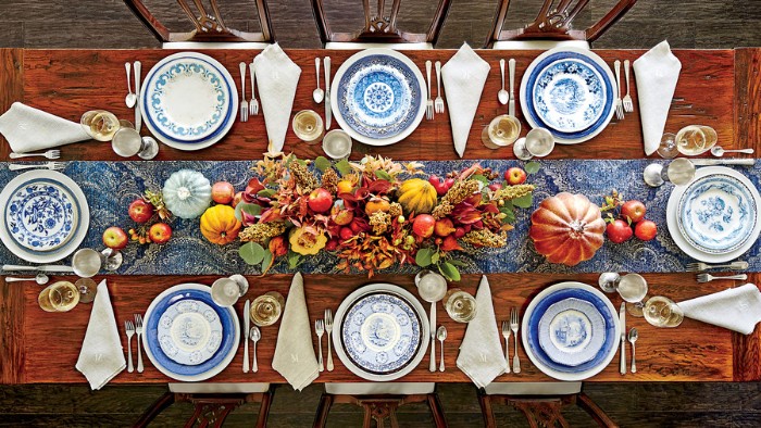 wooden rectangular table, with eight plates, in white and blue, white napkins and silver cutlery, decorative pumpkins and fall leaves, thanksgiving dinnerware