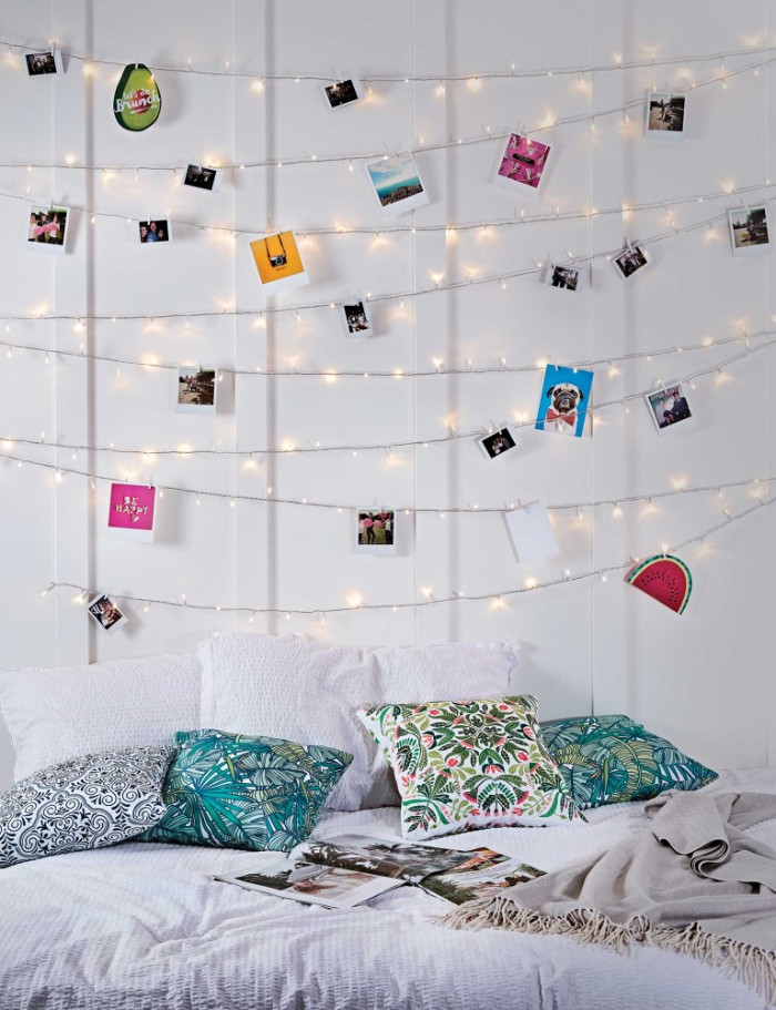 lit string lights, hung on a white wall, and decorated with polaroid photos, and small colorful images, cheap ways to decorate a teenage girl's bedroom, bed with three pillows, and four cushions