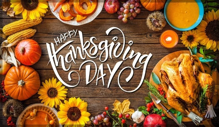 sunflowers and ears of corn, roasted turkey and other dishes, a candle and some grapes, on a wooden surface, with the words happy thanksgiving day overimposed in white