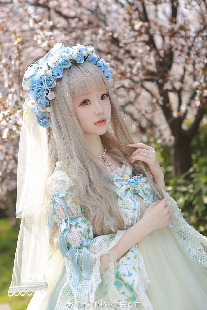 baby blue and white dress, with lace and frills, decorated with ribbons and bows, lolita fashion, worn by a girl, in a long platinum blonde wig, with faux flowers and a veil