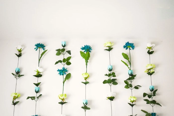 seven columns made of faux flowers, in teal and white, light yellow and pale blue, with long green stems, stuck together, diys for girls, attached to a white wall