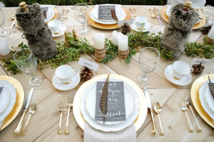 plush dark grey bottle holders, on a festive table, with gold and white plates, topped with black menu cards, and spotted feathers, thanksgiving tablescape, candles and green decorative folliage