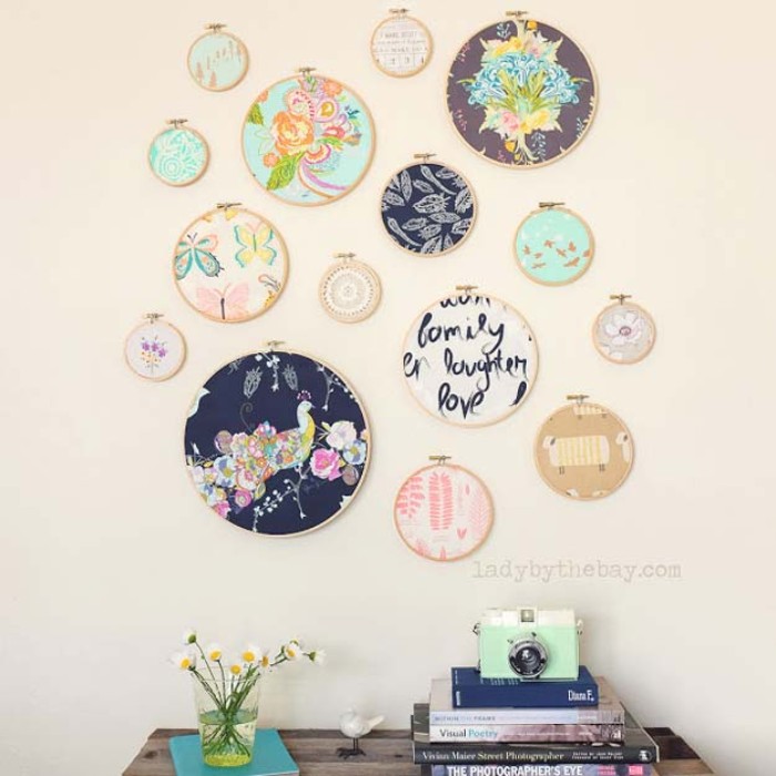 embroidery circles made of wood, featuring pieces of fabric with different prints, and in different colors, hung on a pale cream wall, over a small wooden table