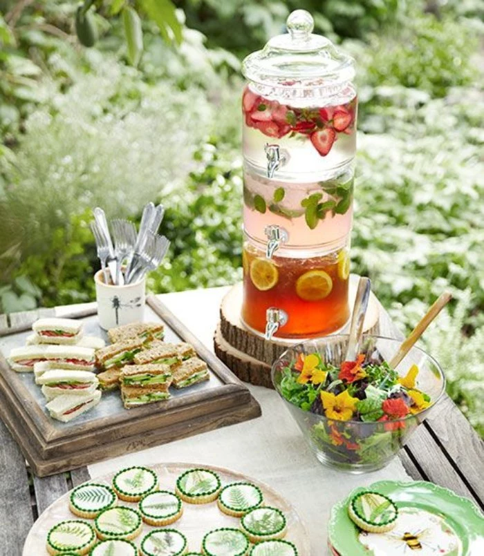 tea garden party, a rustic wooden table, with finger sandwiches, different kinds of lemonade, in a fancy vintage glass dispenser, salad and cookies, 50th birthday party ideas for mom 