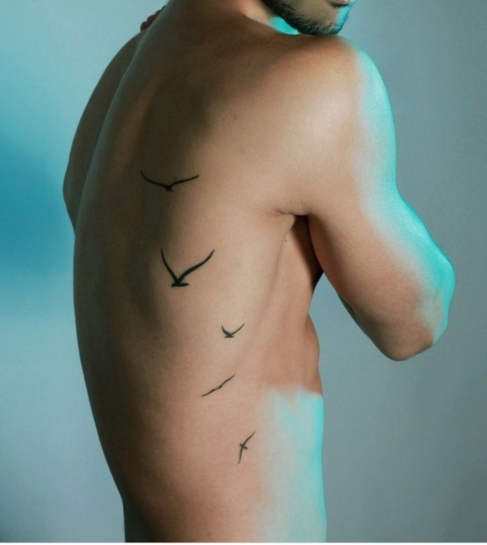 birds in flight, tattooed in black, on the back of a slim, but athletic young man, small meaningful tattoos, symbolizing freedom and lightness
