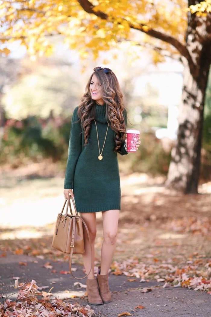 laughing brunette woman, wearing a dark green, turtle neck jumper dress, and beige suede ankle boots, she is holding a matching beige leather bag, and a red coffee cup