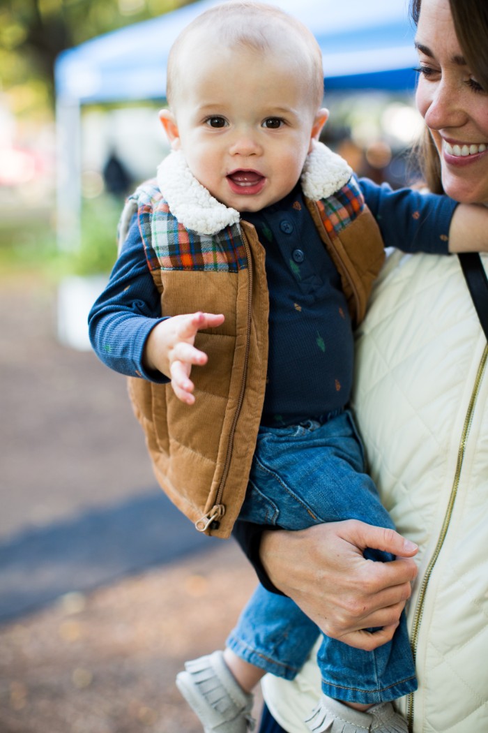 baby thanksgiving outfits, dark navy jumper, and blue jeans, on a small baby boy, wearing a beige gilet, with a white sherling fur trim, and plaid details