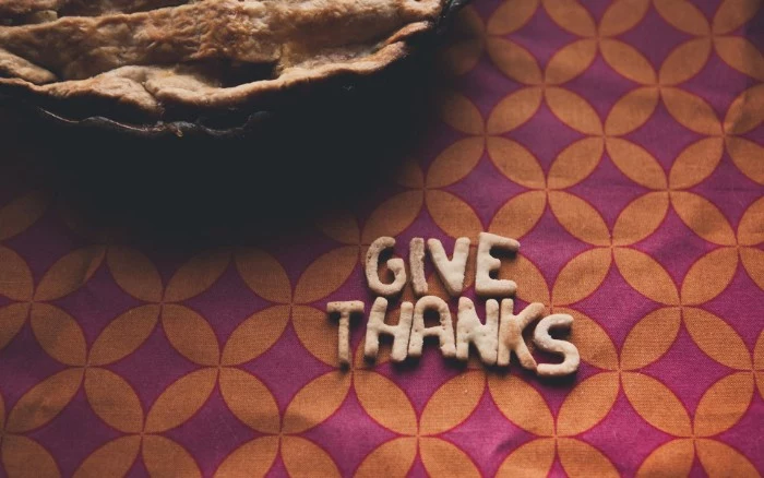 letters made from baked dough, spelling out the words give thanks, on a retro tablecloth, with an orange and purple pattern, and a pie nearby
