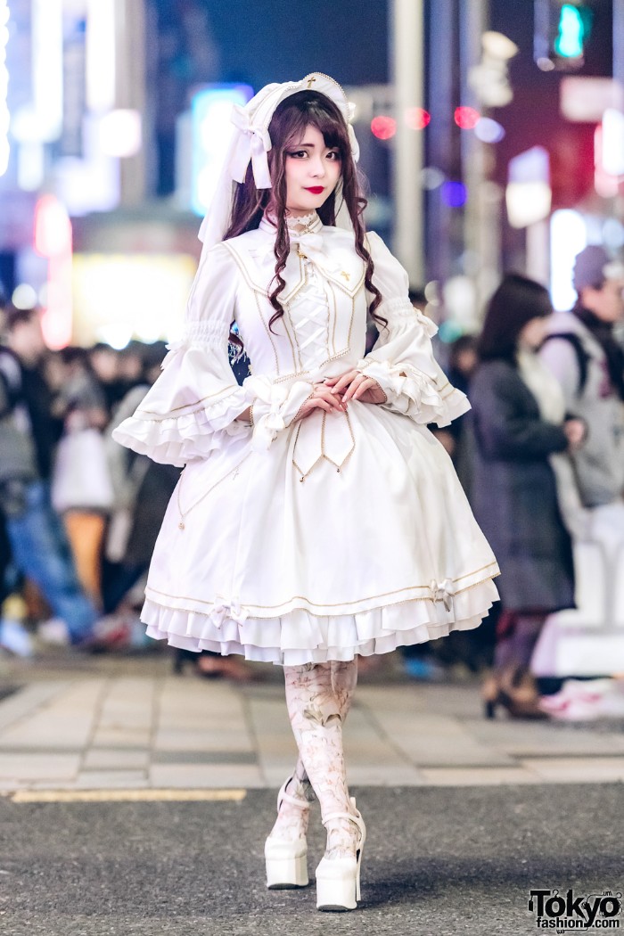 white dress with bell-shaped sleeves, a corset-like lace-up detail, and a large collar, featuring gold details, and cross motifs, define lolita, on a girl, wearing a brunette wig