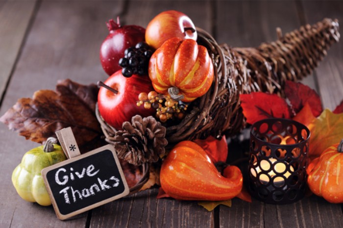 give thanks written in white chalk, on a small black and beige sign, placed near a horn of plenty decoration, filled and surrounded by small faux pumpkins, fall leaves and apples, gourds an pine cones