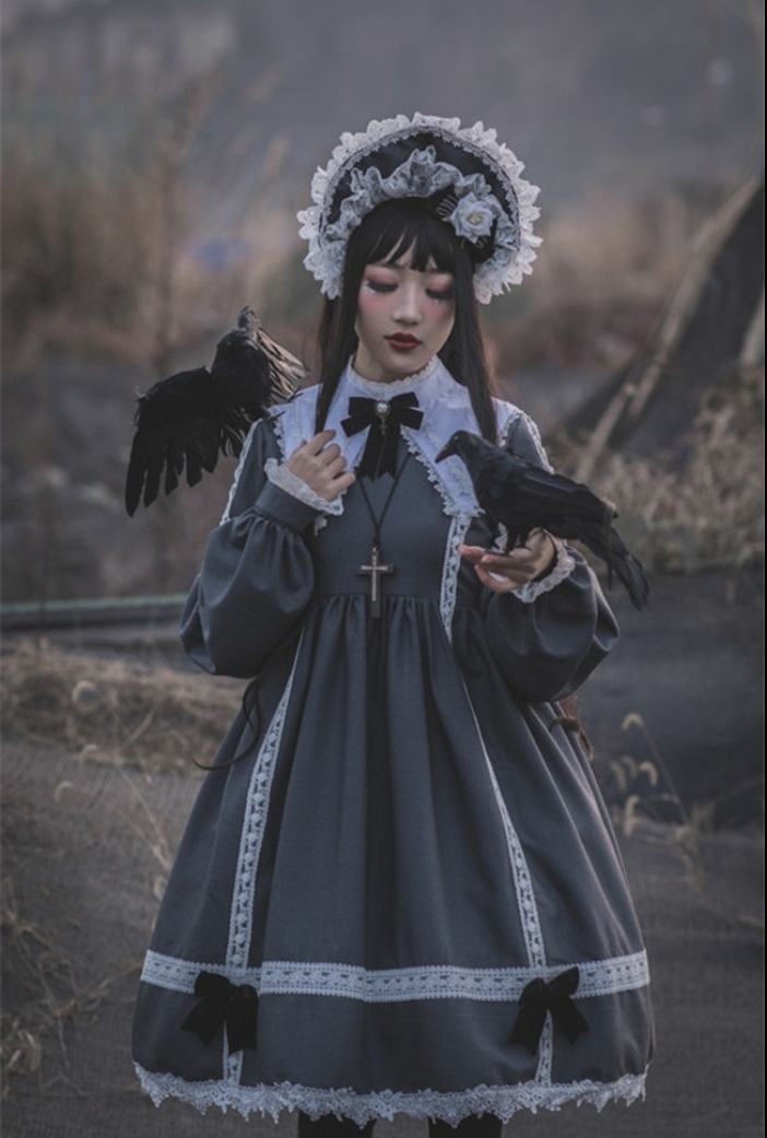 crow props held by a girl, dressed in a grey lolita outfit, with a white collar, lace details and small dark bows, frilly bonnet and a cross necklace