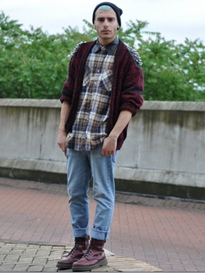 punk and grunge outfit, inspired by 90s bands, featuring light blue ankle jeans, burgundy combat boots, a plaid shirt, and a dark purple cardigan with leather shoulder details, decorated with spikes, on a young man, with light blue hair, and a black beanie hat 