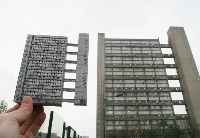 miniature model of the trellick tower, held by a hand, near the real trellic tower, concrete architecture icons