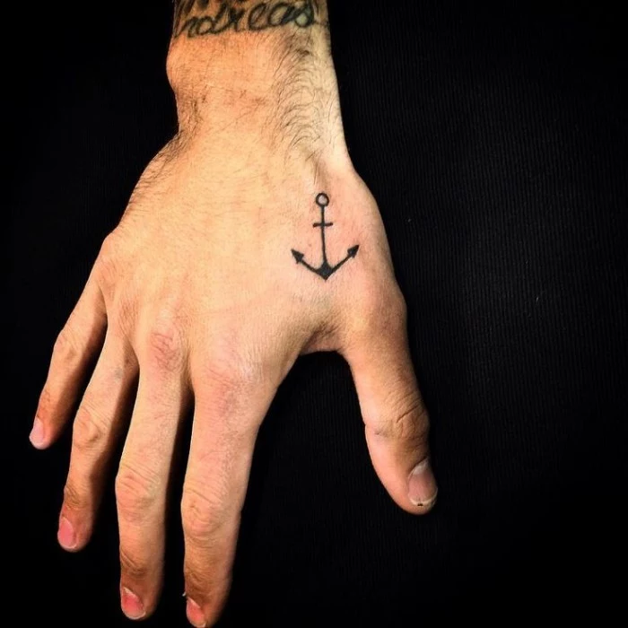 simple anchor in black, tattooed on a man's hand, close to his thumb, small symbolic tattoos, security and stability, black background