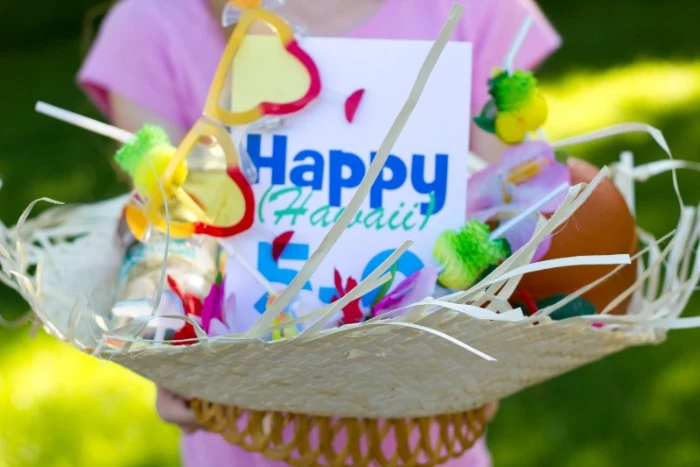 straw hat containing a card, with the inscription happy hawaii 5-0, colorful garlands and sunglasses, 50th birthday colors, held by a girl dressed in pink