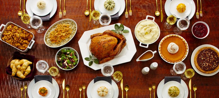 roasted turkey on a white plate, placed on a brown table, and surrounded by different dishes, pies and salads, croissants and sides, thanksgiving wishes, six sets of plates, with gold cutlery