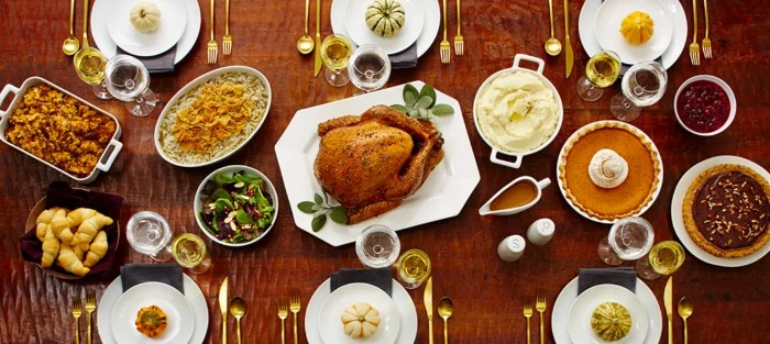 roasted turkey on a white plate, placed on a brown table, and surrounded by different dishes, pies and salads, croissants and sides, thanksgiving wishes, six sets of plates, with gold cutlery