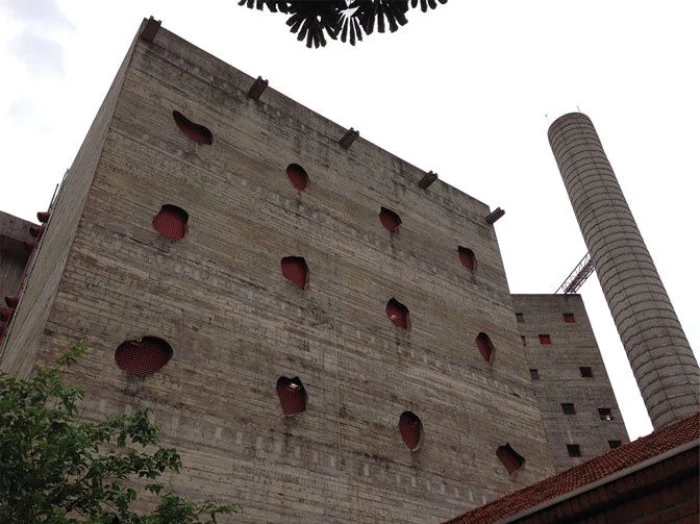sesc pompéia in sao paulo, large brutalist design building, made of brick and concrete, featuring holes in different shapes, and a tall chimney
