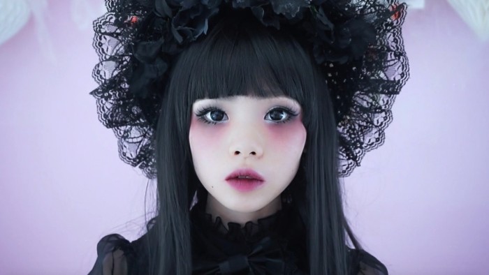 very pale japanese lolita, with pink eyeshadow and lipstick, seen in close up, wearing a semi sheer, frilly blouse and a black lace bonnet