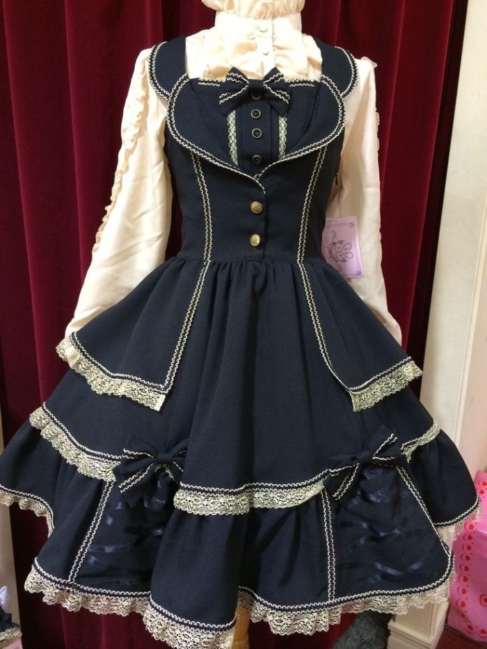 navy blue dress, with lace trims, and ribbon details, decorated with several small bows, worn over a frilly cream shirt, what is lolita fashion