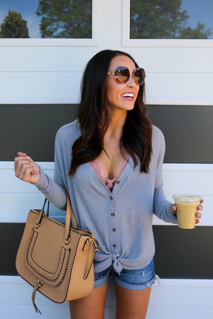 bralette outfit, worn by a smiling brunette woman, with a grey ribbed cardigan, tied in a knot at the bottom, blue denim shorts, and a pink bralette