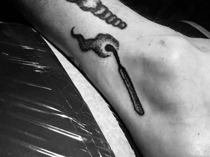 flaming match done in black ink, near another tattoo, on a person's ankle, small tattoos with meaning, on a greyscale photo